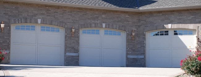 Three white carriage-style garage doors with arched window rows on a brick home