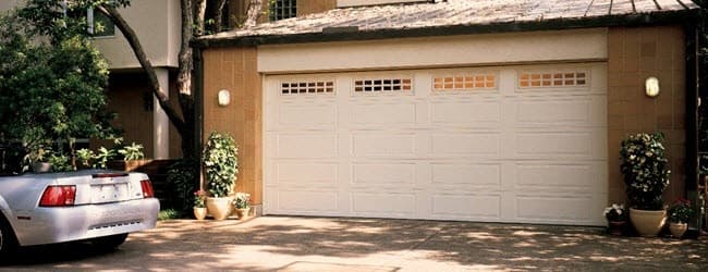White raised-panel garage door with a row of windows on a tan stucco home