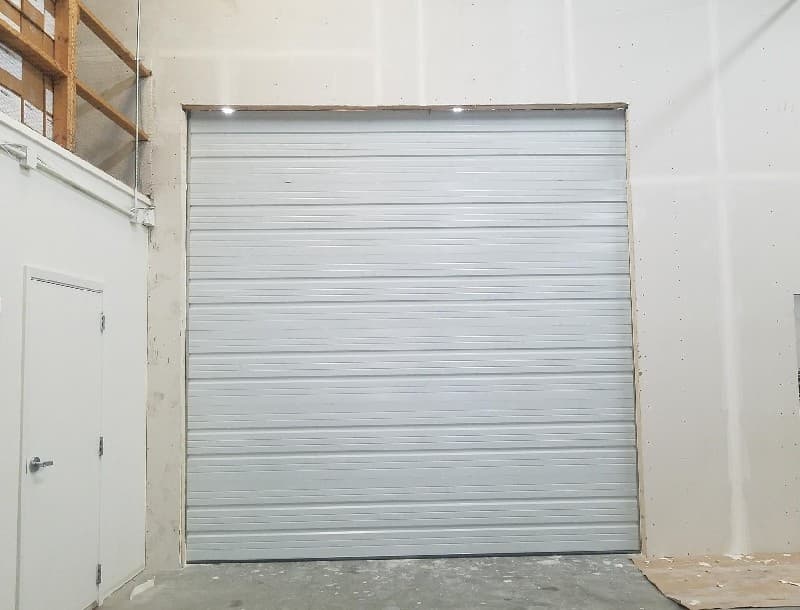 Large white sectional overhead door installed in a commercial unit next to a service entry door