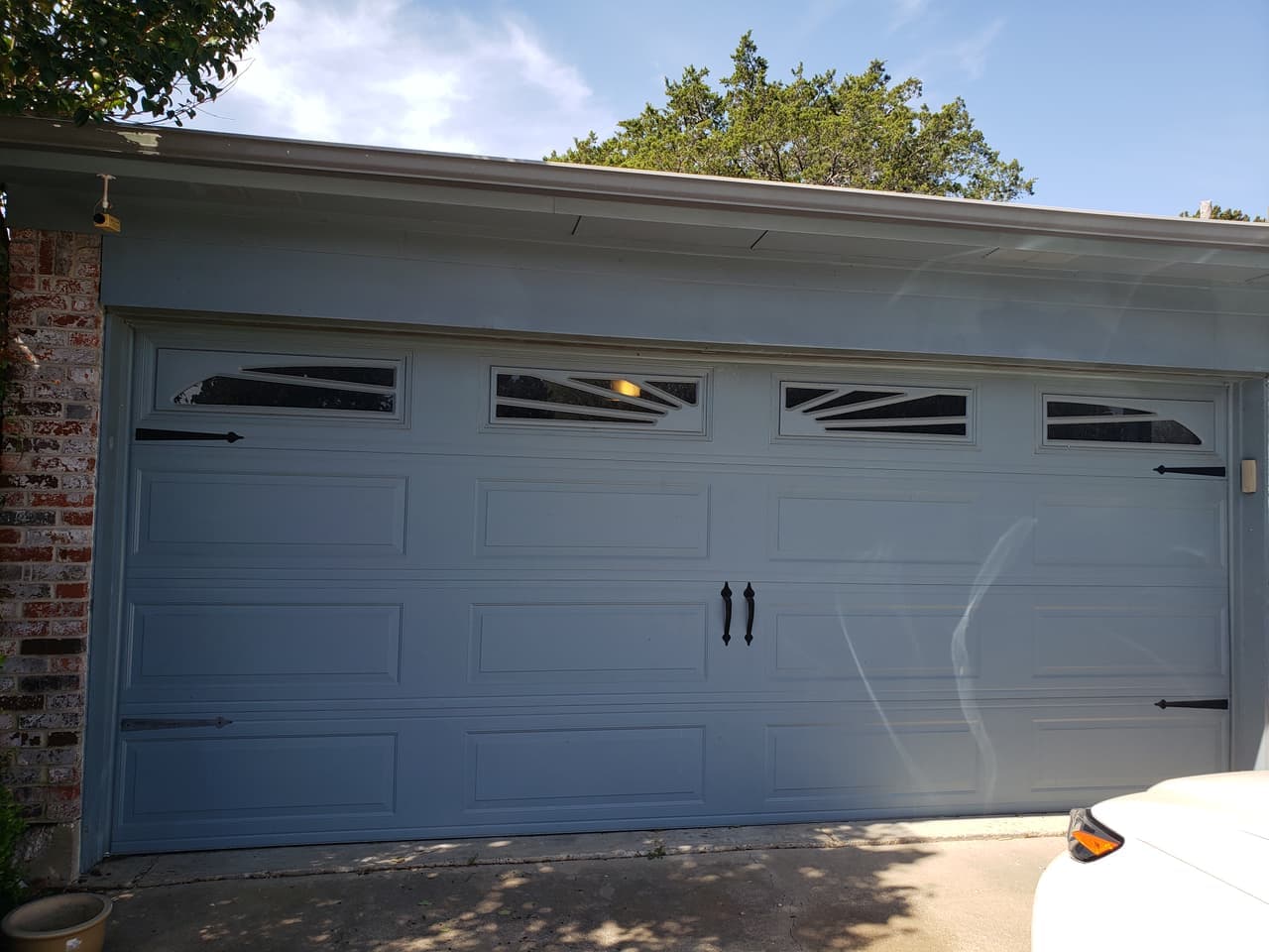 Gray-blue two-car steel garage door with sunburst-style windows and black decorative hardware