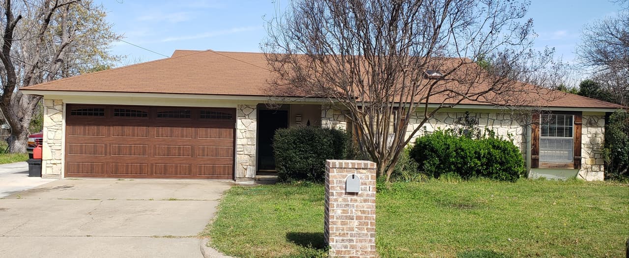 Stone-front ranch home with a new brown wood-look two-car garage door and a brick mailbox