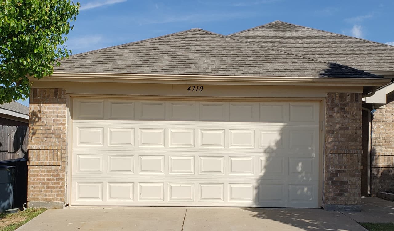 Almond raised-panel two-car garage door on a brick home
