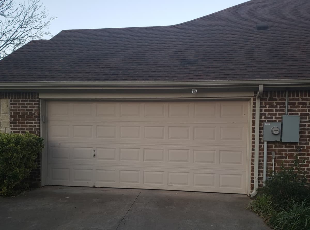 Beige raised-panel two-car garage door on a dark brick home in Granbury, Texas