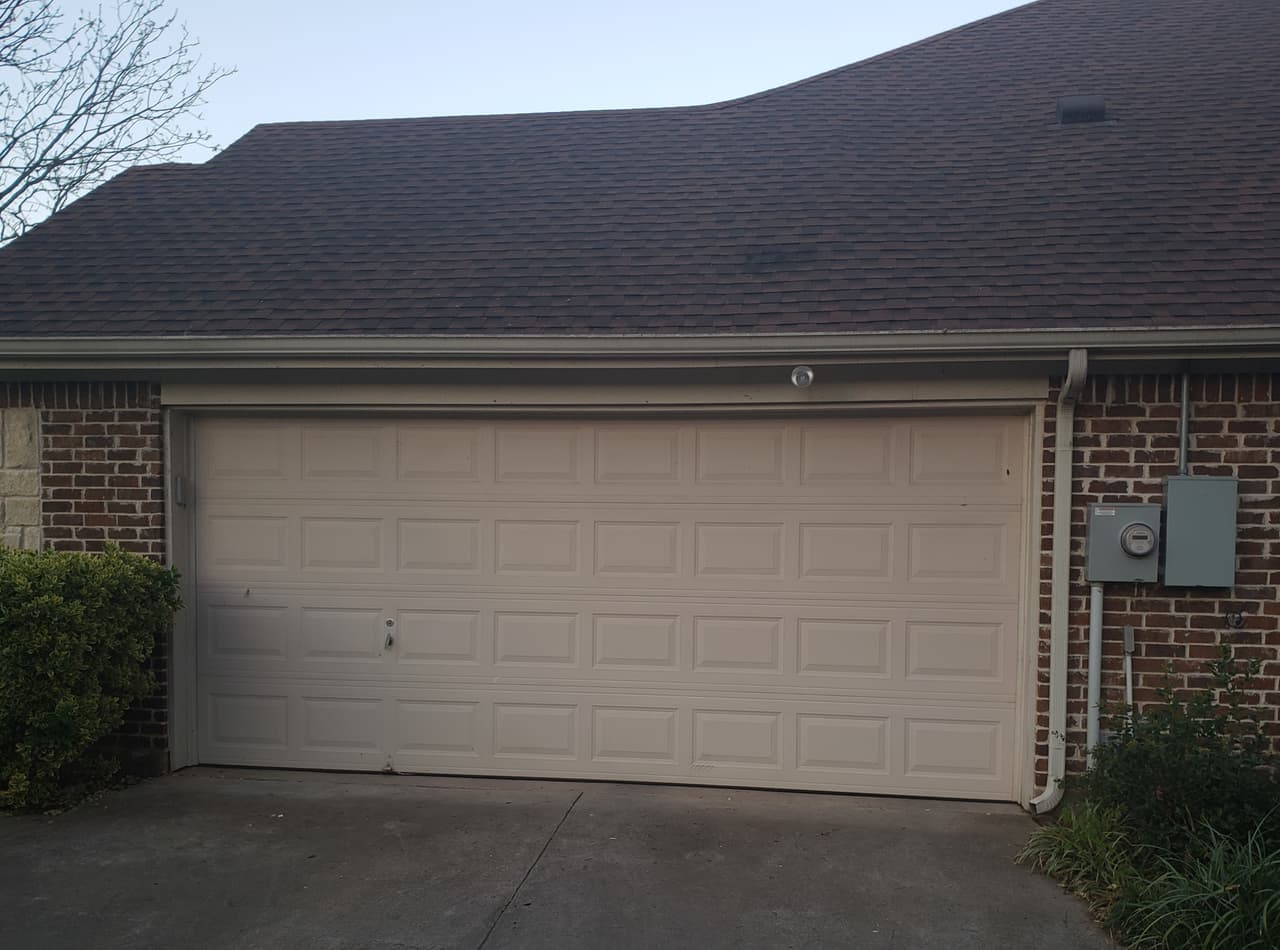 Beige raised-panel two-car garage door on a dark brick home