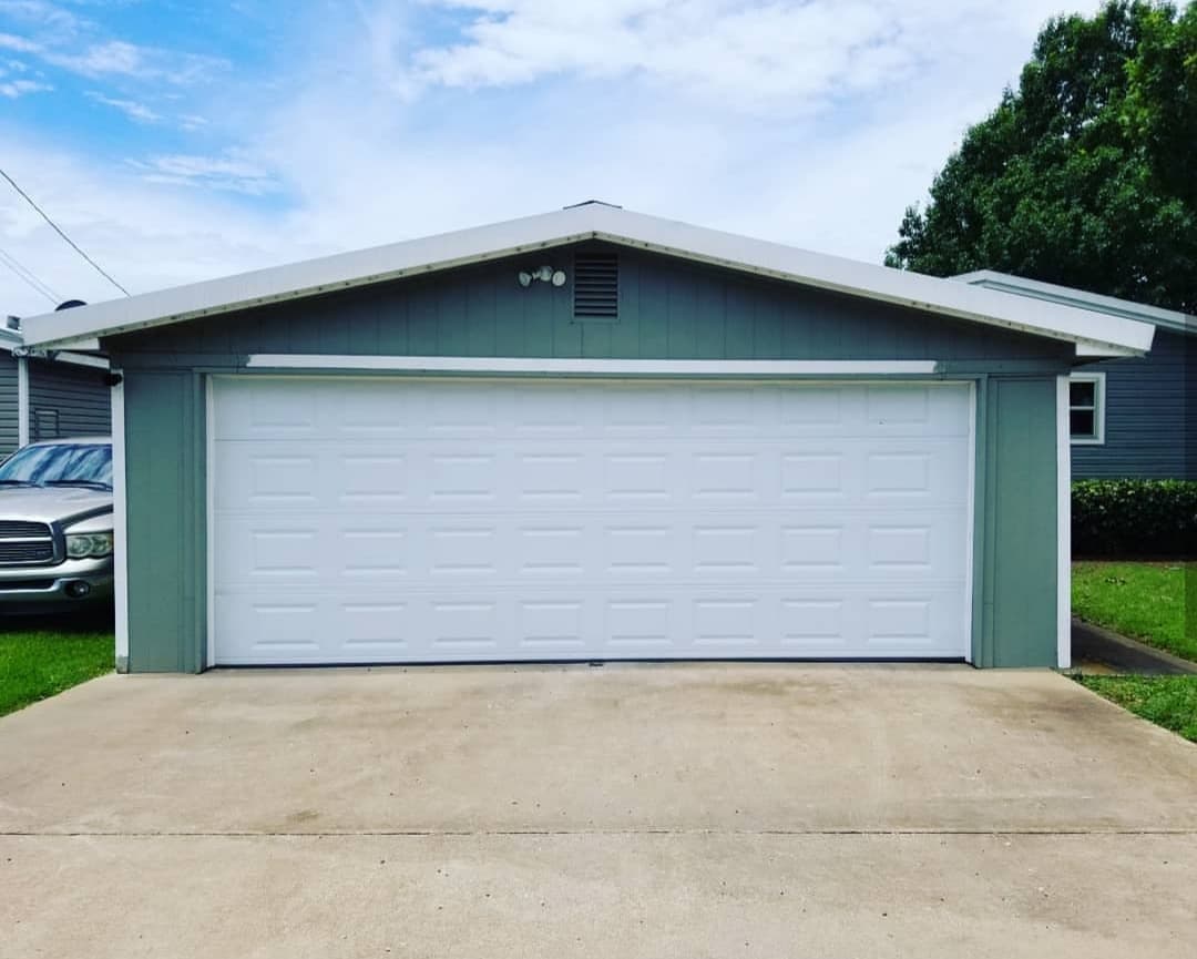 White raised-panel garage door on a green detached two-car garage