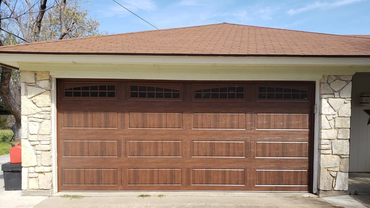 New brown wood-look garage door with arched windows between limestone columns